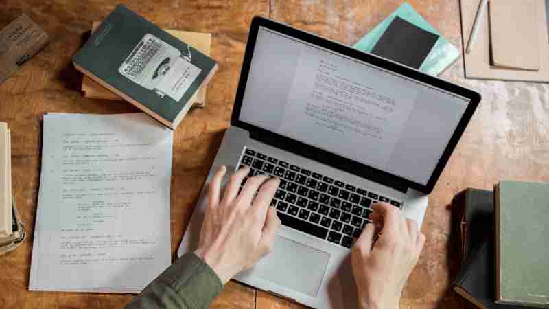 High-angle view of hands typing on a laptop surrounded by books and papers., tags: mastering strategic steps - pexel