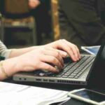 Adult woman typing on a laptop at a desk with a smartphone and documents., tags: digital - pexel